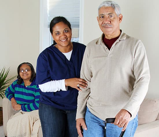A caregiver stands beside a man and a woman in their living room