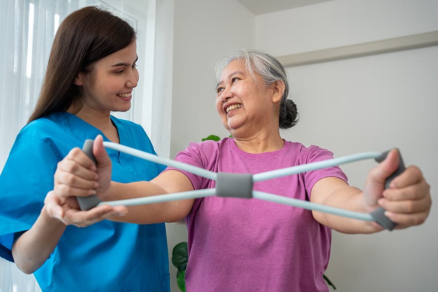 A caregiver and a woman laugh together while stretching resistance bands