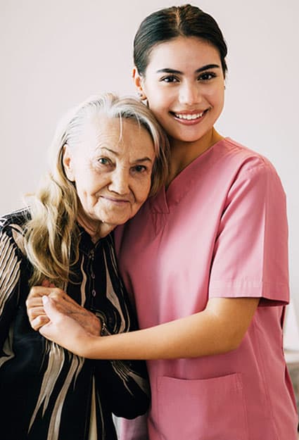 A caregiver and a woman share a warm embrace, both smiling
