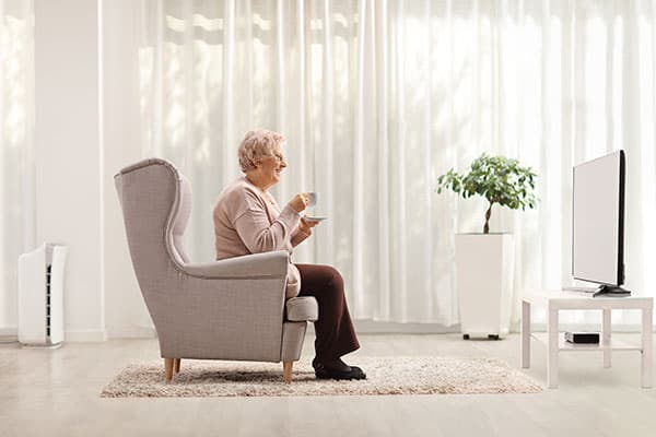 A woman relaxes in an armchair with a warm drink, a television across her bright living room